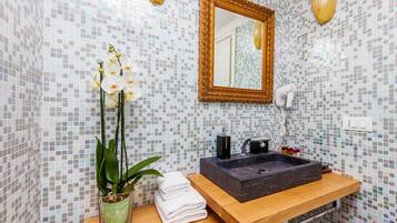 A bathroom with a mosaic tile wall, a wooden vanity with a black sink, a gold-framed mirror, and a potted orchid plant.