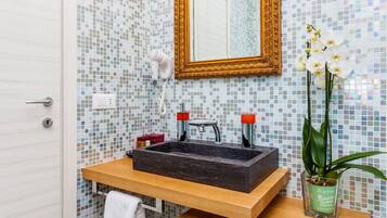 Un baño con pared de mosaicos, tocador de madera, lavamanos, espejo y una orquídea en maceta.