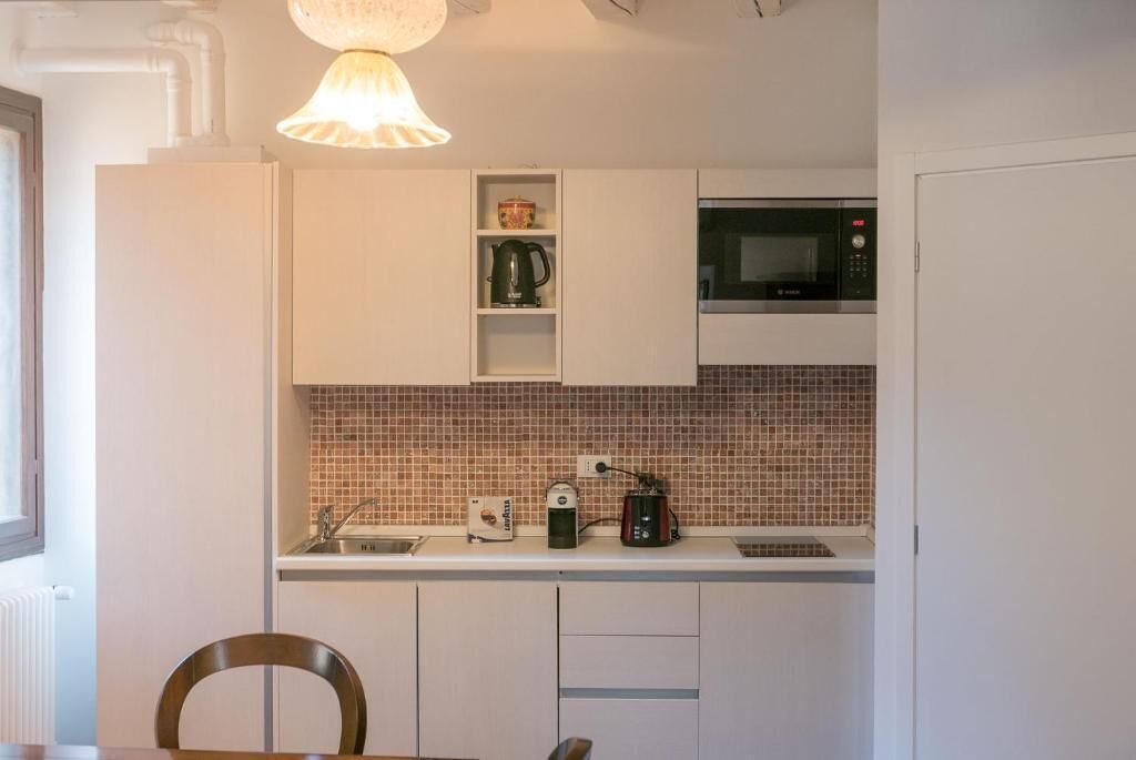 Cocina compacta con armarios blancos, microondas, tetera y lavabo.
