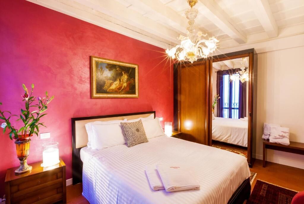 Ein Hotelzimmer mit einem großen Bett, einem Gemälde an der Wand, einer Kristallleuchtre und einem Spiegel.