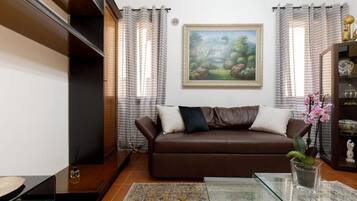 Un salón con un sofá de cuero marrón, una mesa de centro de vidrio, un cuadro enmarcado en la pared y una planta en maceta sobre la mesita auxiliar.