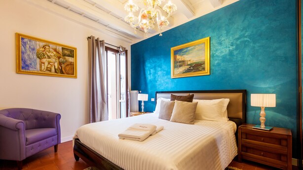 A bedroom with a large bed, a purple armchair, a blue accent wall, and a chandelier. - Residenza Vescovado (Vicenza)
