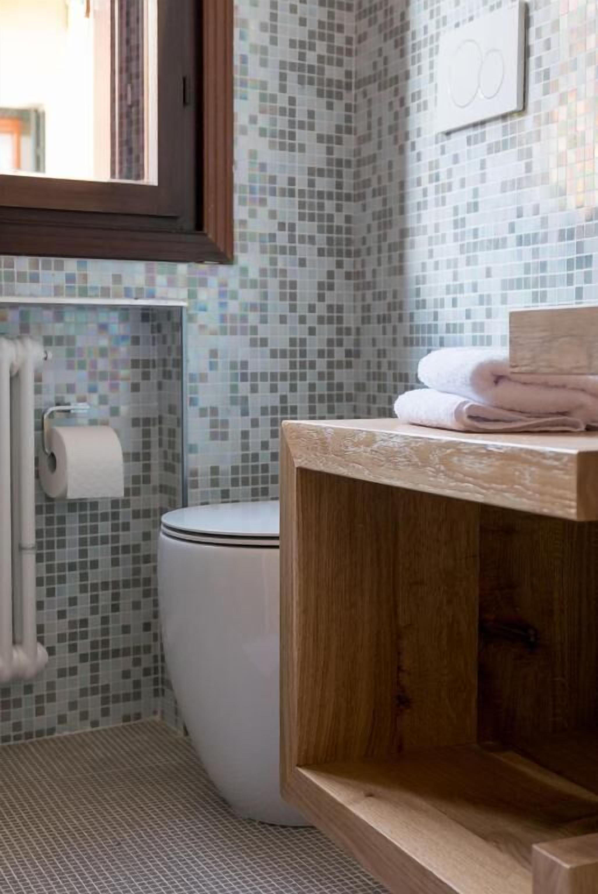 Ein Badezimmer mit Toilette, Toilettenpapier, einem Holzwaschtisch und einer gefliesten Wand.