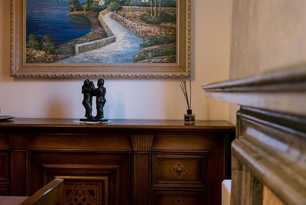 Un aparador de madera con un cuadro enmarco de un paisaje costero, una pequeña escultura y un florero decorativo.