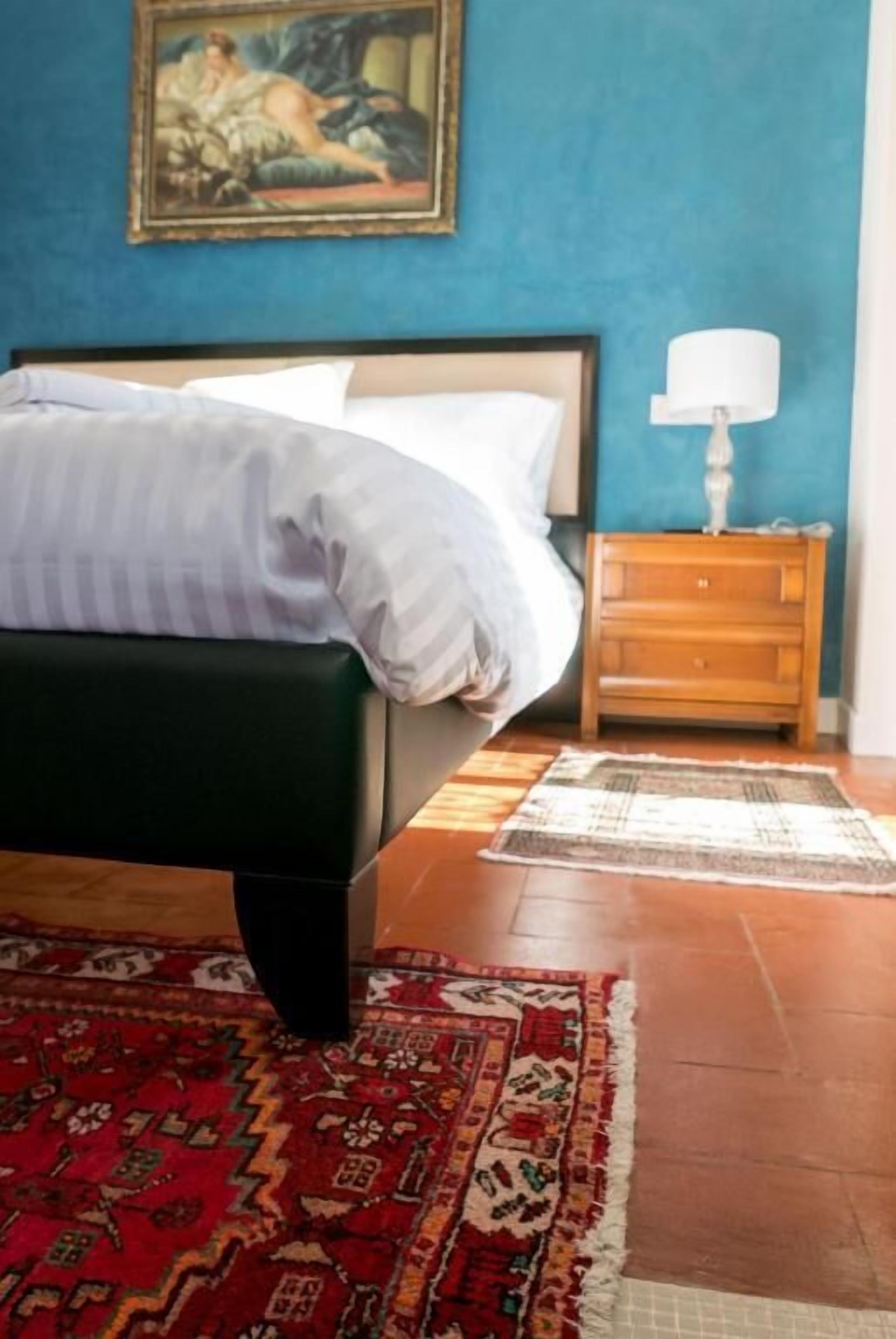 A bedroom with a bed, a nightstand, a lamp, and a painting on the wall.