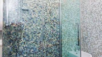 A shower with a glass door, a tiled wall, and a white sink.