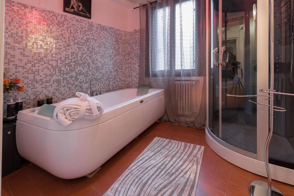 Une salle de bain moderne avec une baignoire sur pieds, une douche à parois de verre et un mur décoré d’une mosaïque de carreaux.