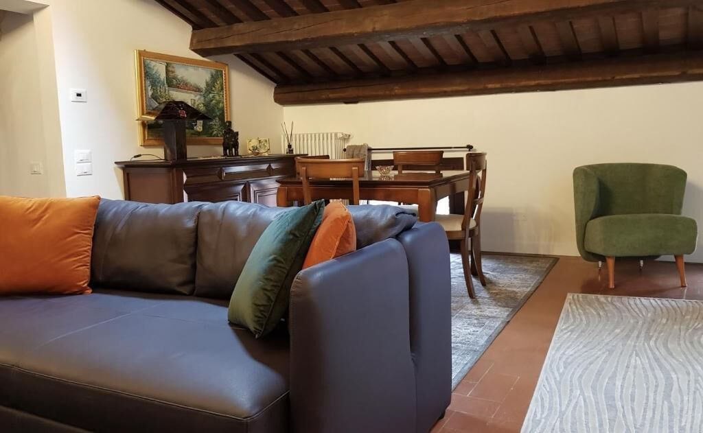 Un soggiorno con un divano in pelle scura, una poltrona verde, un tavolo da pranzo in legno con sedie e un quadro appeso al muro.