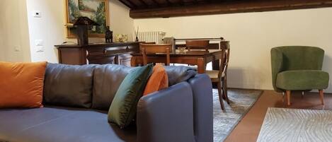 Una sala de estar con un sofá de cuero oscuro, un sillón verde, una mesa de comedor de madera con sillas y un cuadro en la pared.