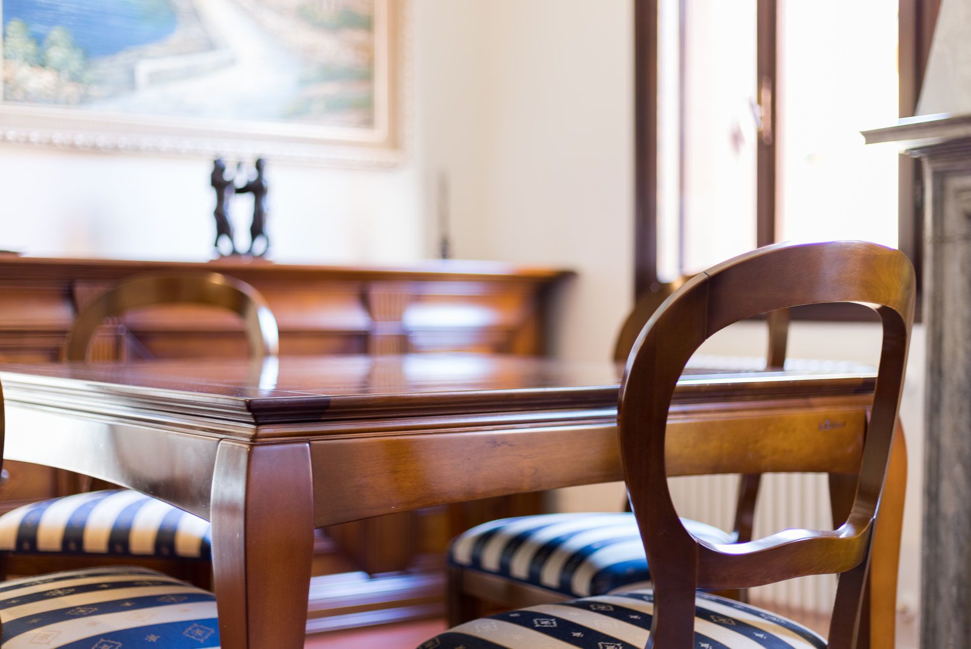 A dining table with chairs, a painting on the wall, and a fireplace.