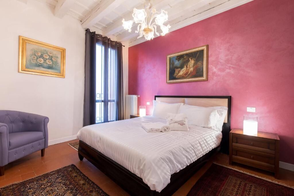 A bedroom with a bed, a nightstand, a chair, and a chandelier.