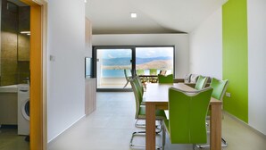 A modern dining area with a view of a lake and mountains, green chairs, and a wooden table. - Nice apartment in Pag with house sea view (Pag)