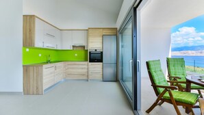 A modern kitchen with wooden cabinets and a green backsplash, a built-in oven, and a large window overlooking a scenic view. - Nice apartment in Pag with house sea view (Pag)