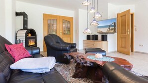 Een woonkamer met een open haard, leren banken, een houten salontafel en een groot raam met uitzicht op het strand.