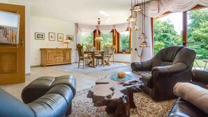 Een woonkamer met een open haard, leren banken, een eethoek met een tafel en stoelen, en uitzicht op groen buiten.