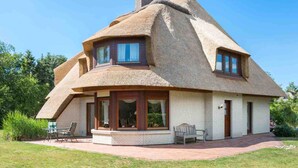 Een rieten dak huis met een bakstenen gevel, een overdekte veranda met zitplaatsen en een heldere lucht.