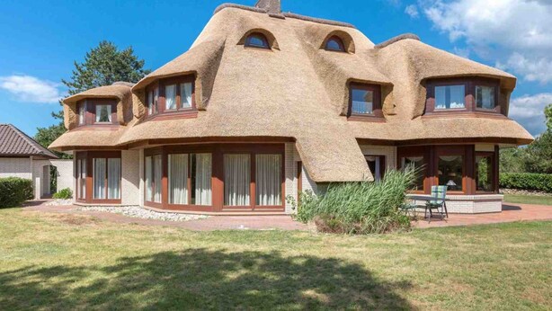 Een huis met een unieke architectuur, herkenbaar aan de ronde, rieten daken en grote ramen.