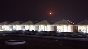 A series of tents with a flat roof, arranged in a row, each with a small table and chairs in front. - Dynasty Desert Camp (Jaisalmer)