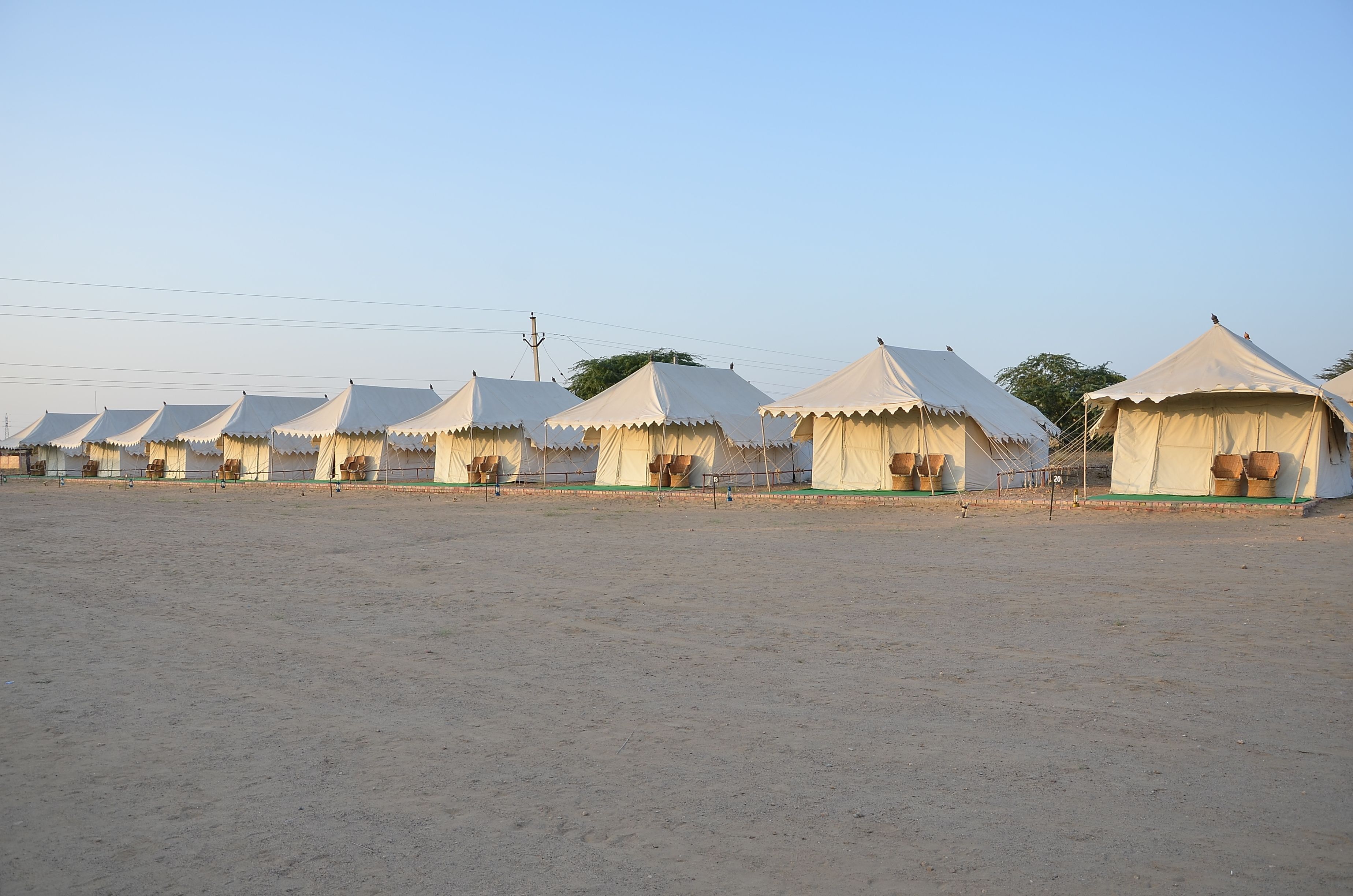 A row of beige tents with a simple, functional design, arranged in a linear fashion on a sandy ground.