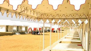 A row of tents with a patterned canopy, a sandy ground, and a few people in the background. - Dynasty Desert Camp (Jaisalmer)