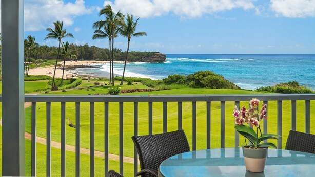 A balcony with a view of a beach, palm trees, and the ocean.
