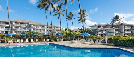 A hotel with a swimming pool, palm trees, and lounge chairs.