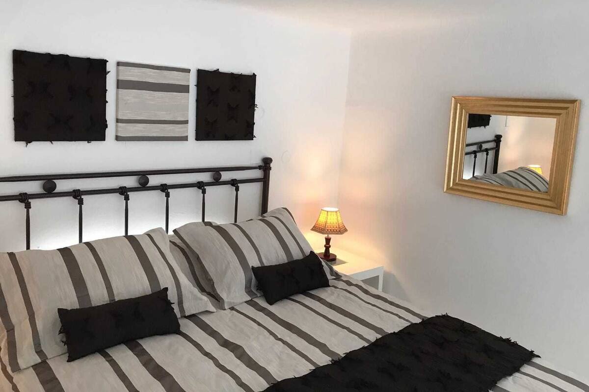 A bed with striped bedding and a headboard, a bedside lamp, and two wall-mounted artworks.