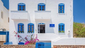 Un edificio blanco con detalles azules, un letrero que dice "Milos Inn" y un muro de piedra al frente.