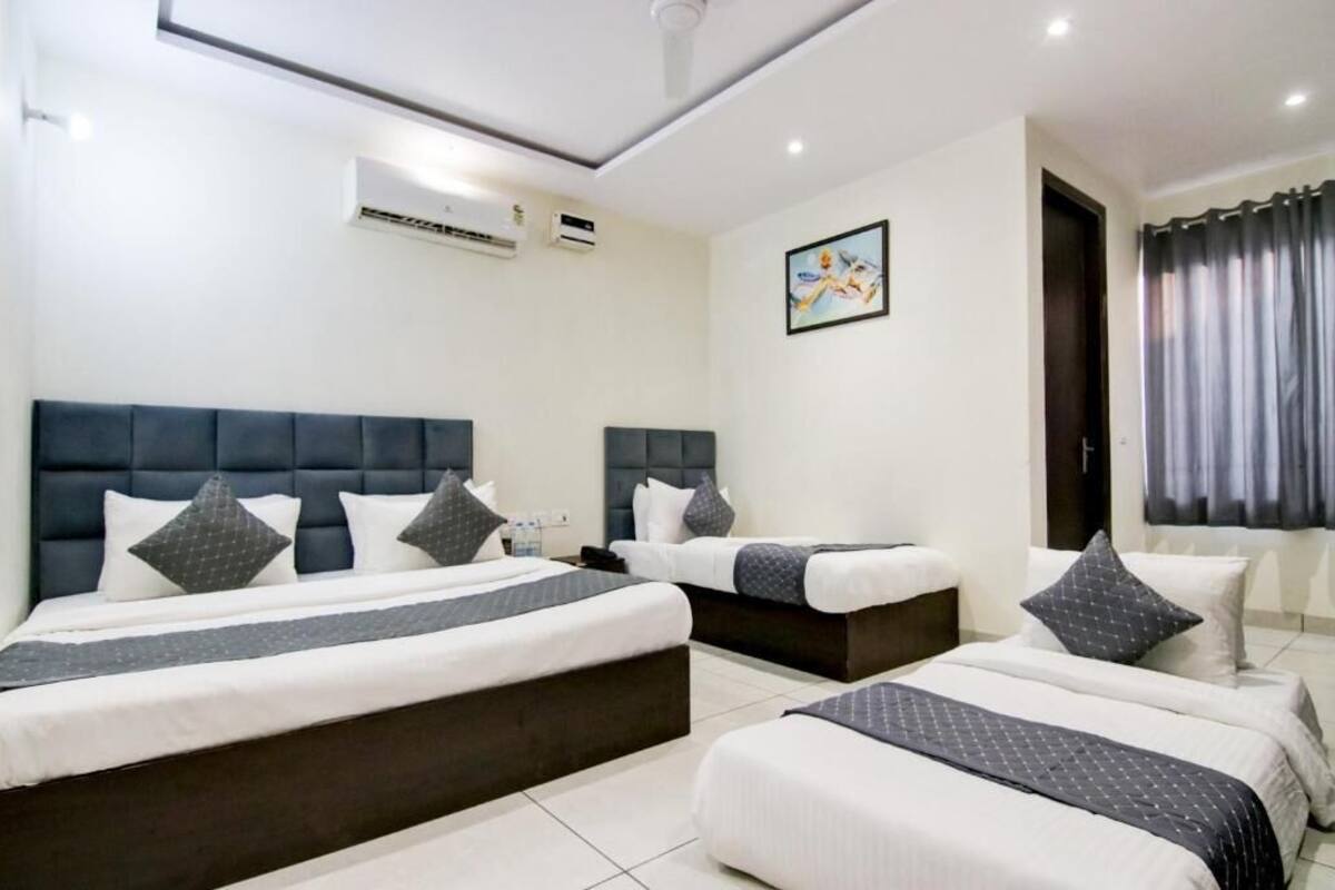 A hotel room with three beds, a large window with curtains, and an air conditioning unit on the wall.