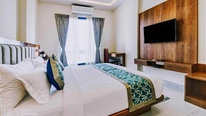 A hotel room with a large bed, a flat-screen TV mounted on a wooden panel, and a window with curtains.