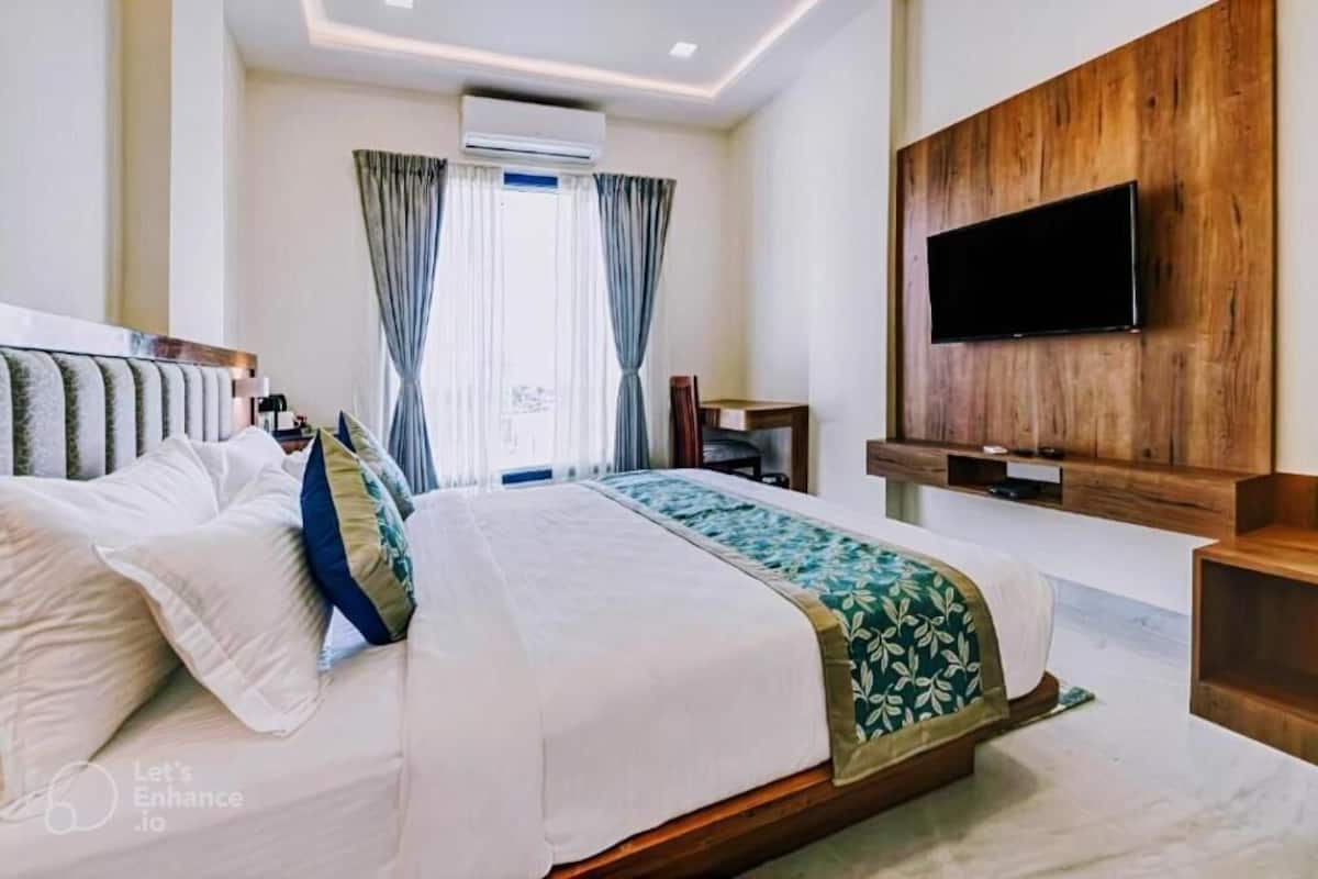 A hotel room with a large bed, a flat-screen TV mounted on a wooden panel, and a window with curtains.