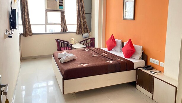 Une chambre d’hôtel équipée d’un lit, d’un bureau, d’une chaise, d’une fenêtre avec des rideaux, d’un climatiseur et d’un téléphone fixé au mur.