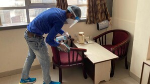 Une personne est en train de nettoyer une table dans une pièce qui contient une fenêtre, une chaise et un climatiseur fixé au mur.