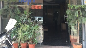 L’entrée d’un hôtel, avec une porte en verre, des plantes en pot et une moto Honda garée à l’extérieur.
