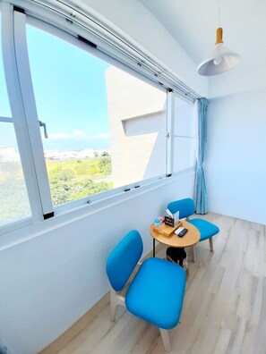 A modern room with a large window, two blue chairs, a small round table, and a hanging pendant light.