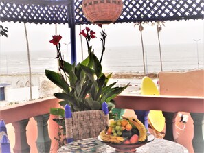 A balcony with a potted plant, a bowl of fruit, and a view of the sea. - Riad Dar Statia (El Jadida)