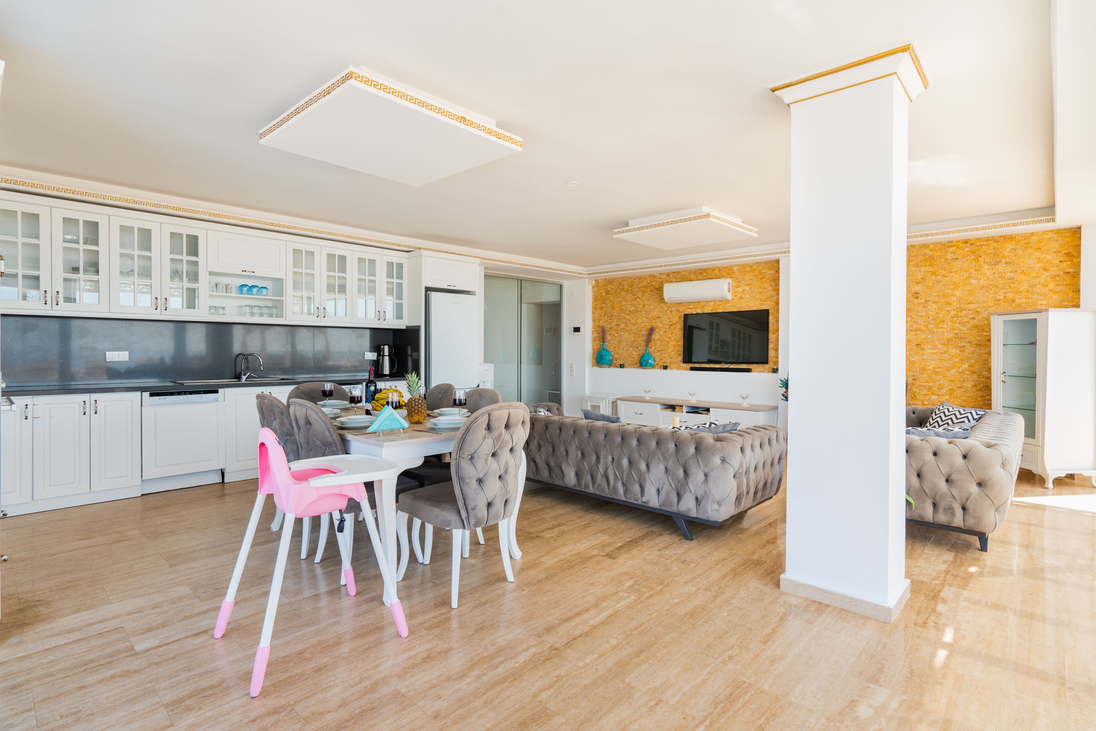 Una cocina moderna con armarios blancos, una zona de comedor con sillas rosadas y un salón con un sofá capitonado.