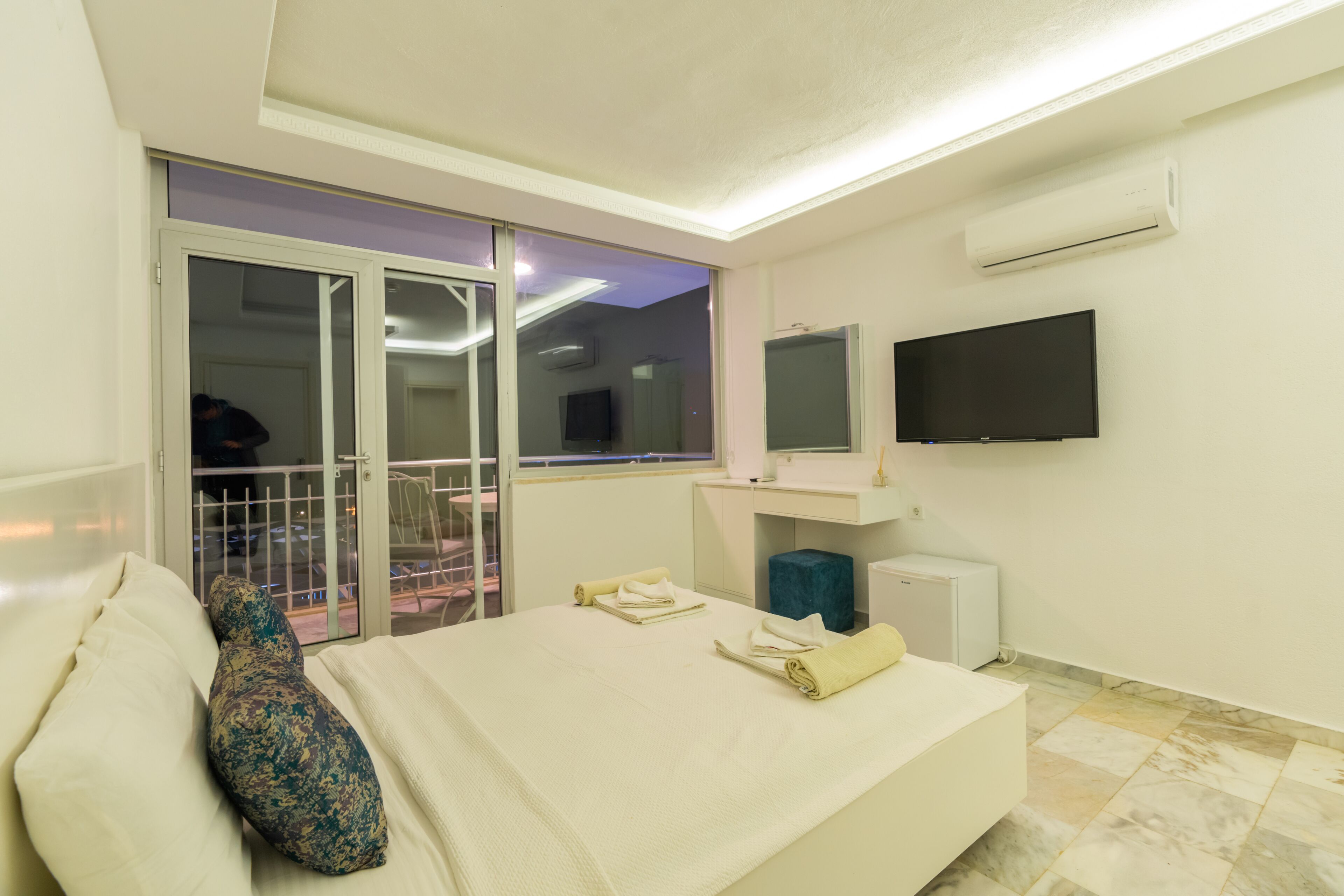 Une chambre d’hôtel équipée d’un lit, d’un téléviseur fixé au mur, d’une fenêtre donnant sur l’extérieur et d’une porte coulissante menant à un espace extérieur.