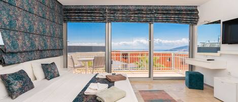 A hotel room with a large bed, a balcony with a view, a TV, and a small desk.