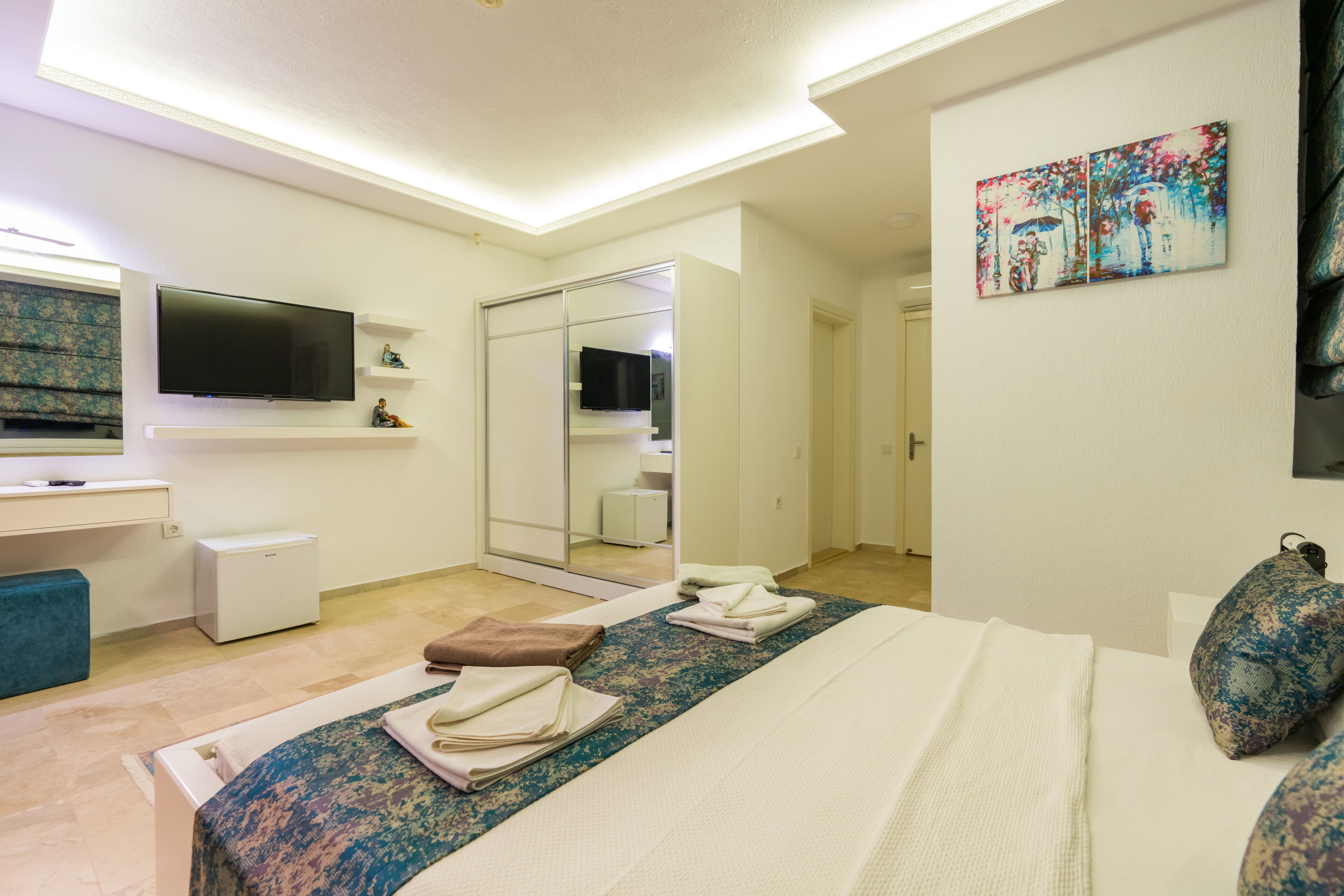 Quarto de hotel com uma cama, televisão na parede, espelho e um quadro.