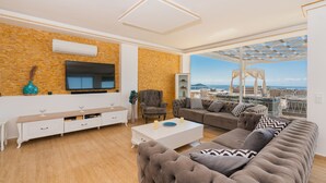A modern living room with a large window, a flat-screen TV, a sofa, and a coffee table. - Infinity Villa Kalkan (Kas)