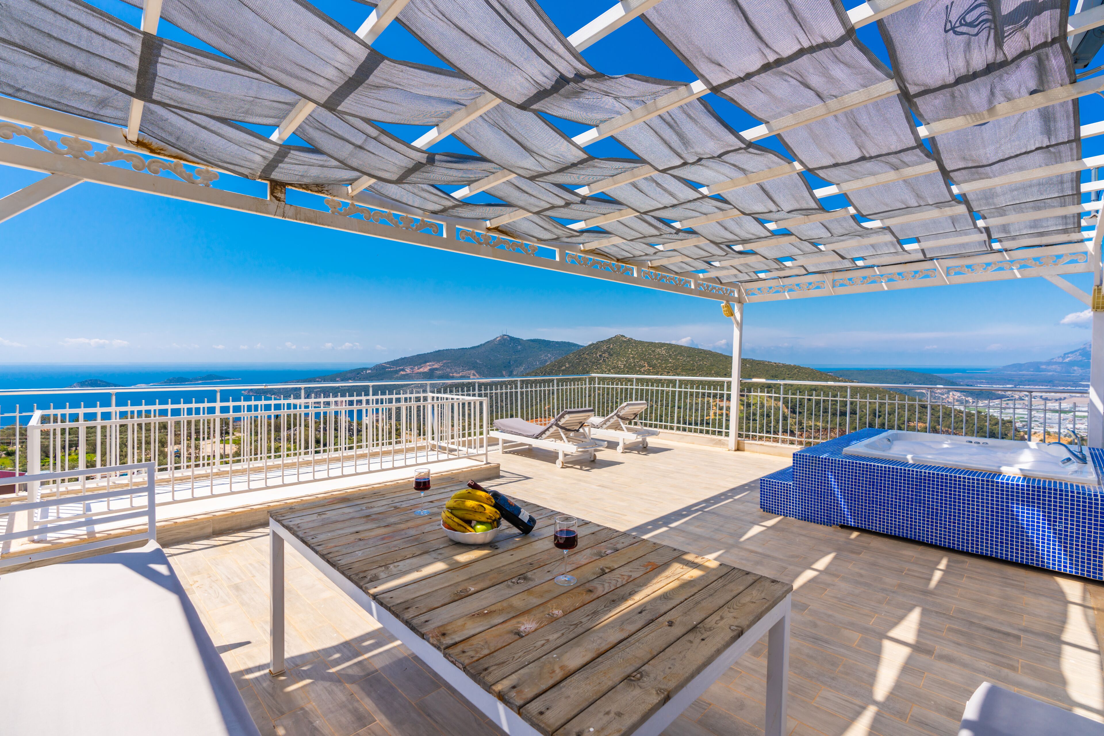 A wooden deck with a hot tub, lounge chairs, and a view of the sea.