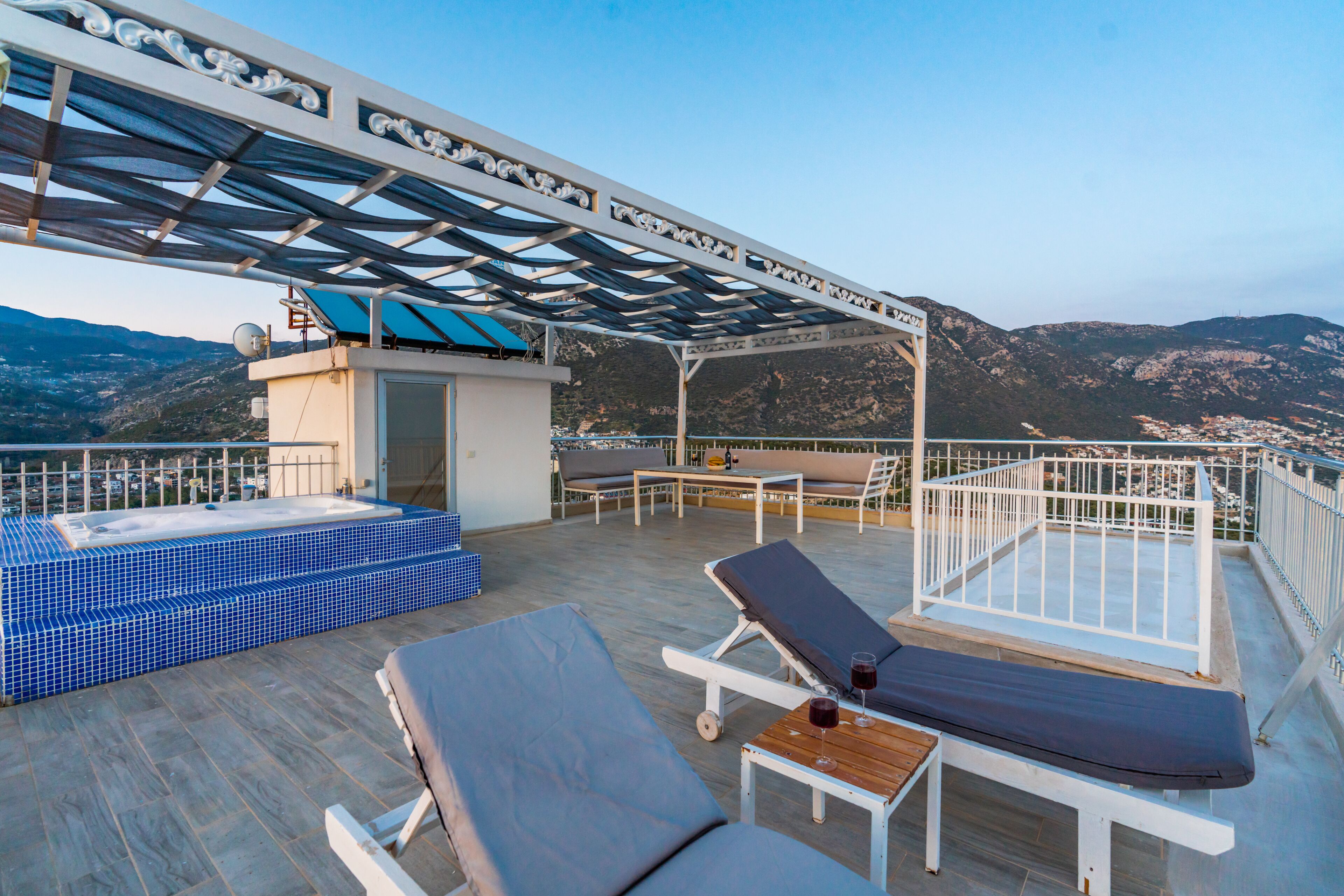 En tagterrasse med liggestole, jacuzzi og et pergolaoverdækket område.