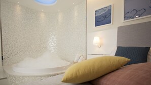 A modern bedroom with a large bed, a built-in bathtub, and a wall-mounted lamp. - Al Chiar di Luna (Monte di Procida)