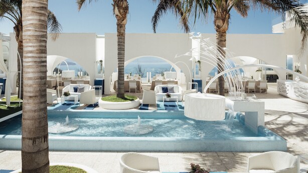 A pool area with lounge chairs and a hot tub, surrounded by palm trees and white architecture. - Al Chiar di Luna (Monte di Procida)
