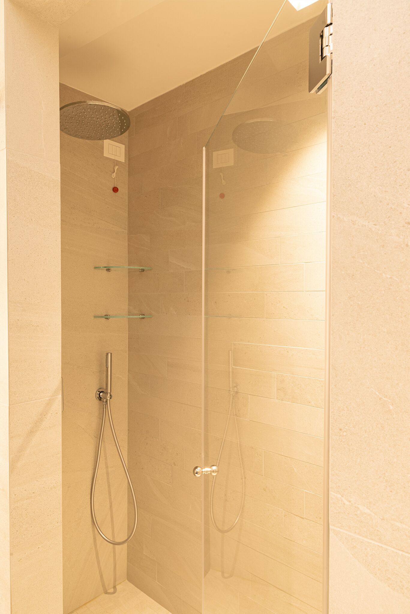 A glass-enclosed shower with a handheld showerhead and a wall-mounted faucet.