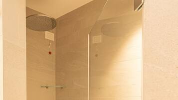 A glass-enclosed shower with a handheld showerhead and a wall-mounted faucet.
