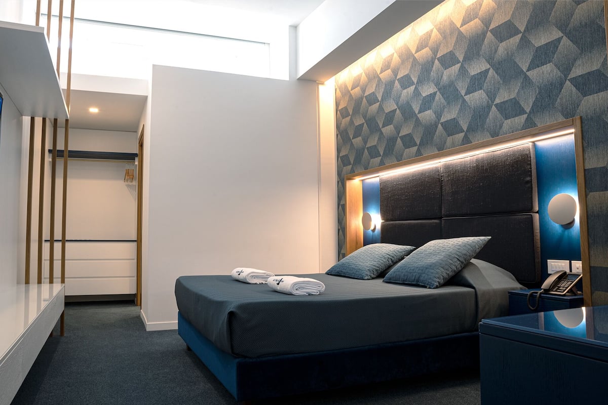 A modern hotel room with a bed, bedside table, and a wall with geometric patterned wallpaper.