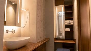 Un baño moderno con un lavamanos blanco tipo recipiente, un espejo y estantes empotrados con toallas dobladas.