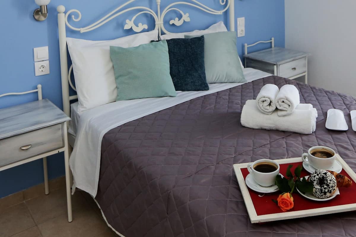 A neatly made bed with a quilted cover, two bedside tables, a wall-mounted painting, and a tray with breakfast items.